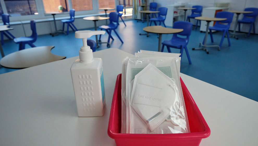 Mascarillas y gel desinfectante en la mesa del profesor de un aula