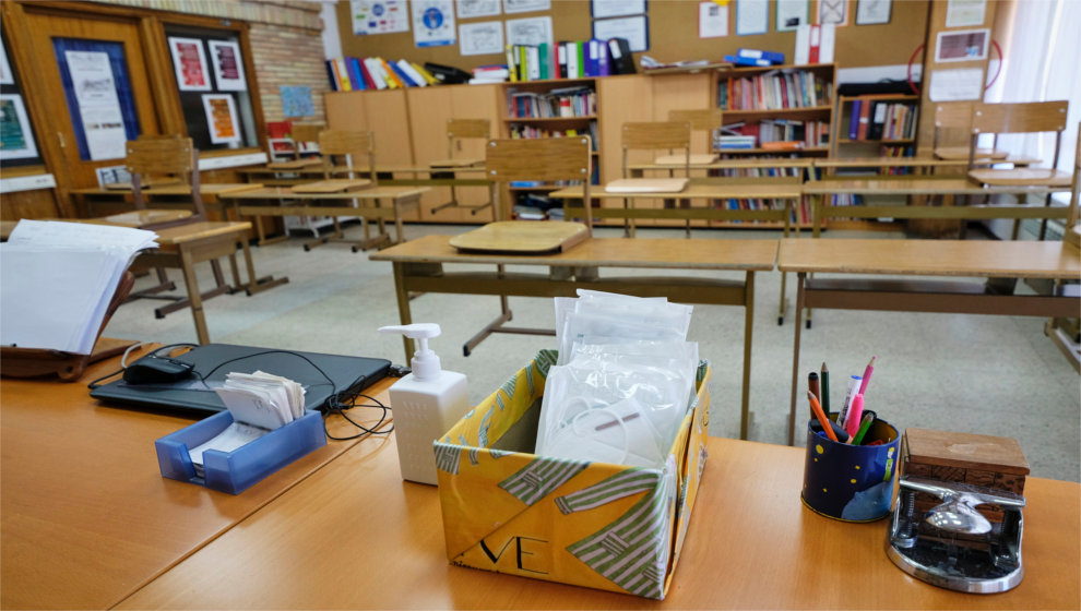 Mascarillas y gel desinfectante en la mesa del profesor de un aula