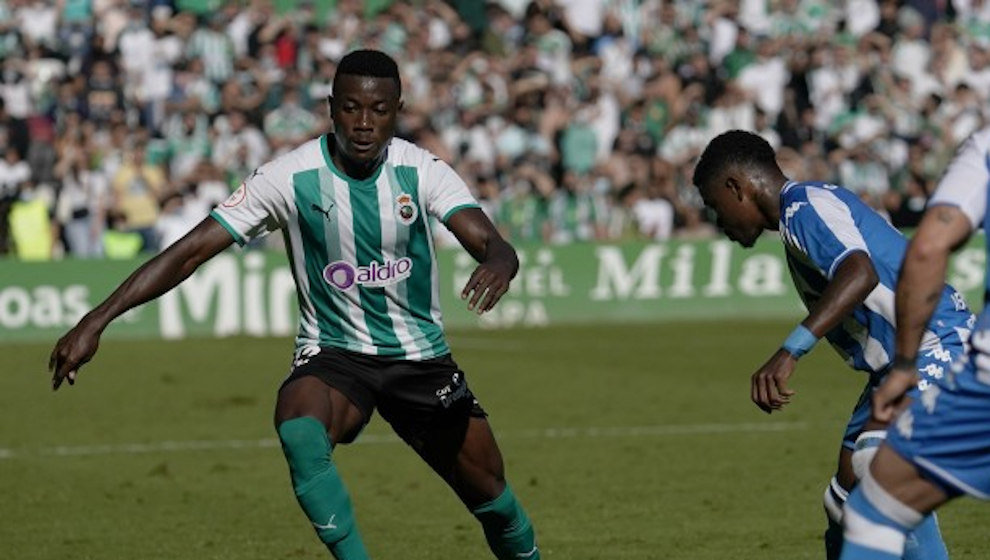 Futbolista del Racing conduce el balón ante la presencia de un jugador del Deportivo