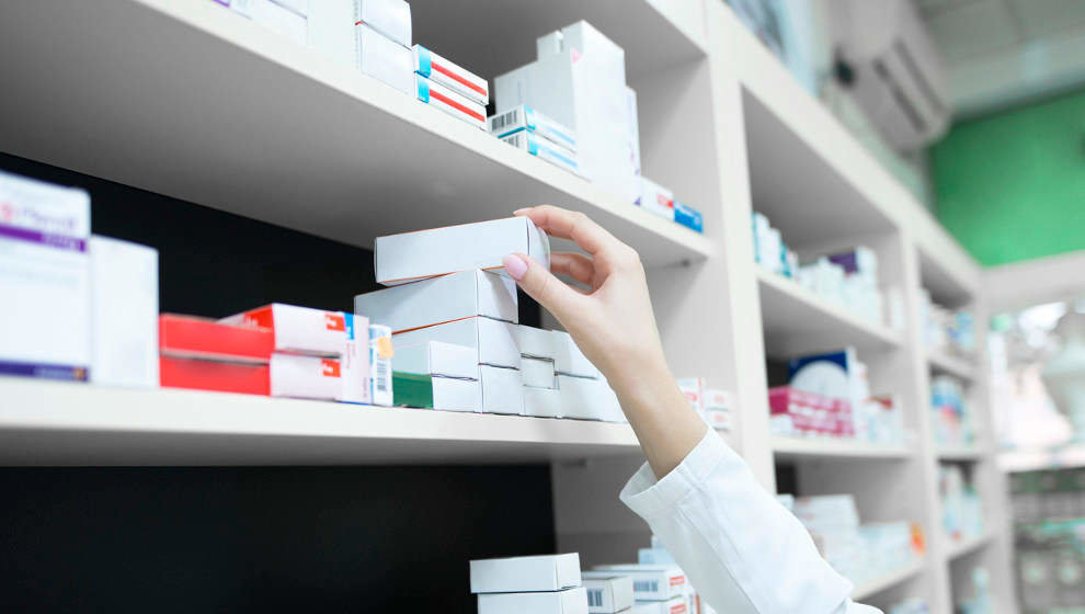 Closeup view of pharmacist hand taking medicine box from the shelf in drug store.