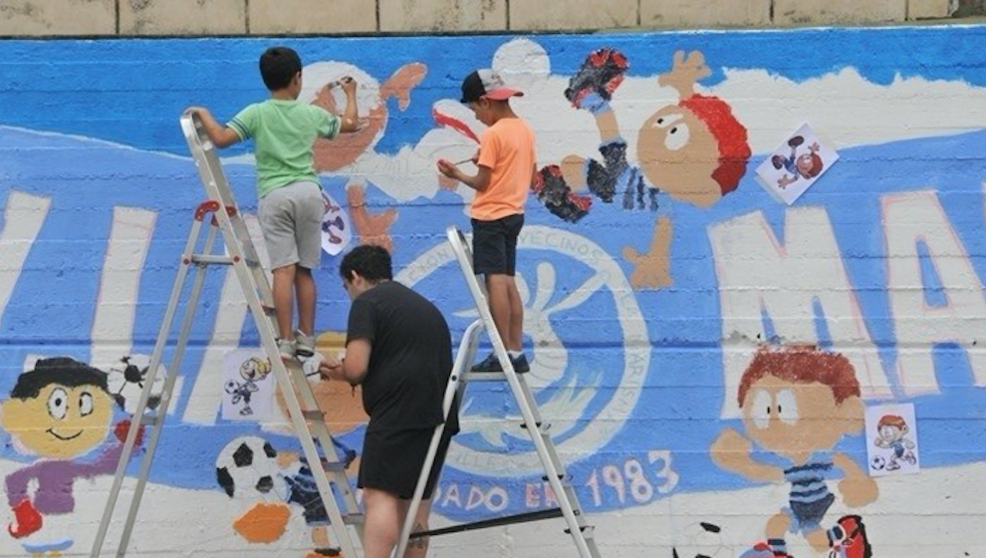 : Niños realizando un mural en la pista deportiva de La Marisma en Astillero