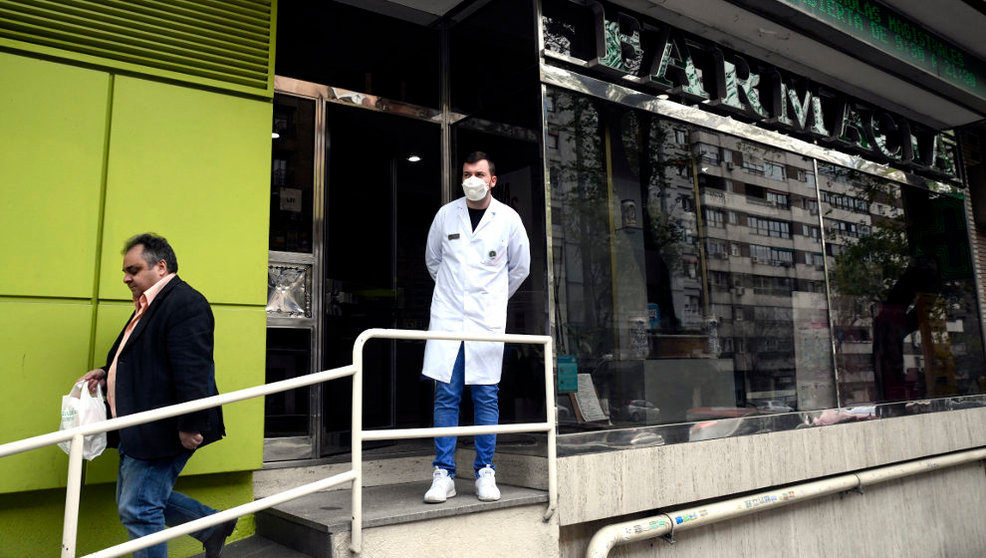 Un farmacéutico protegido con mascarilla en la puerta de una farmacia
