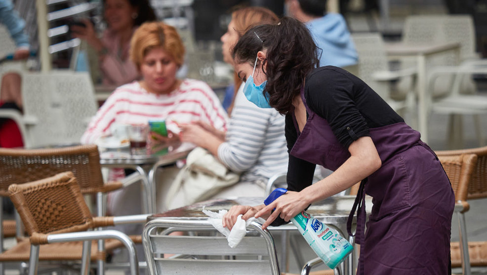 Una trabajadora desinfecta las mesas y sillas de una terraza
