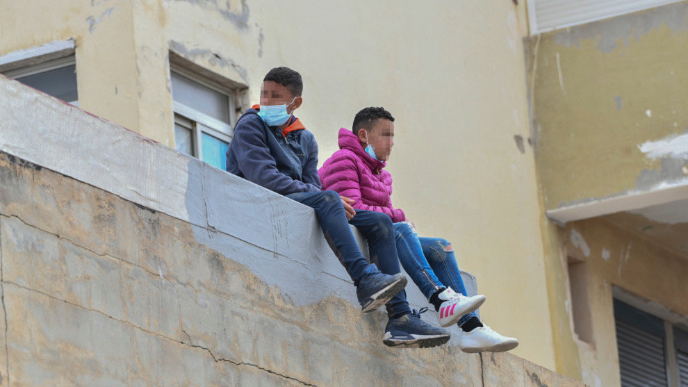 Dos niños sentados sobre un muro en la nave de primera acogida del polígono del Tarajal