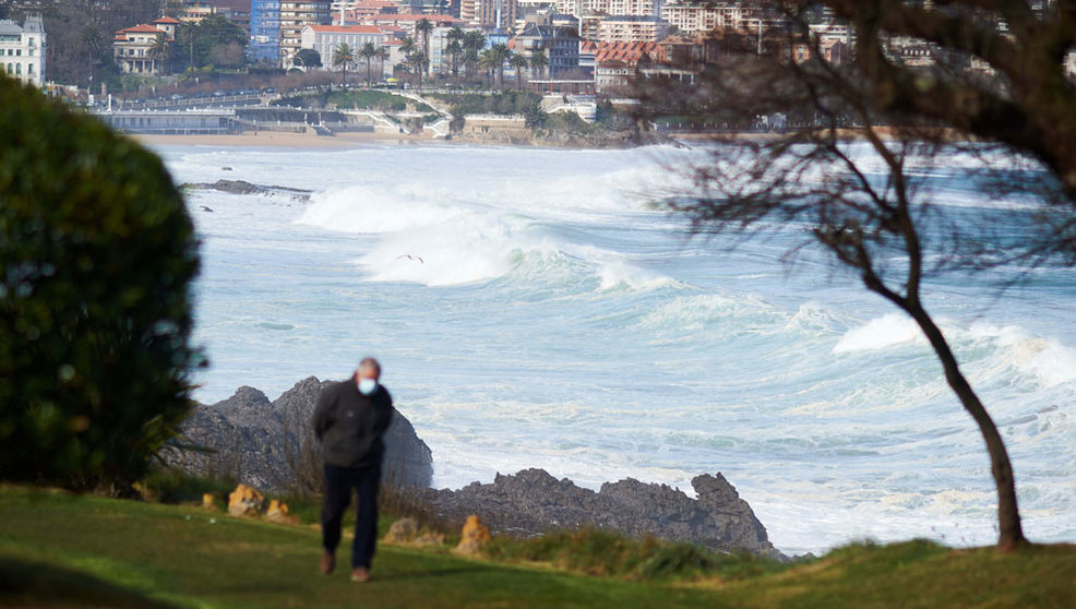 Una personas camina cerca de la playa donde se puede observar el fuerte oleaje en Santander