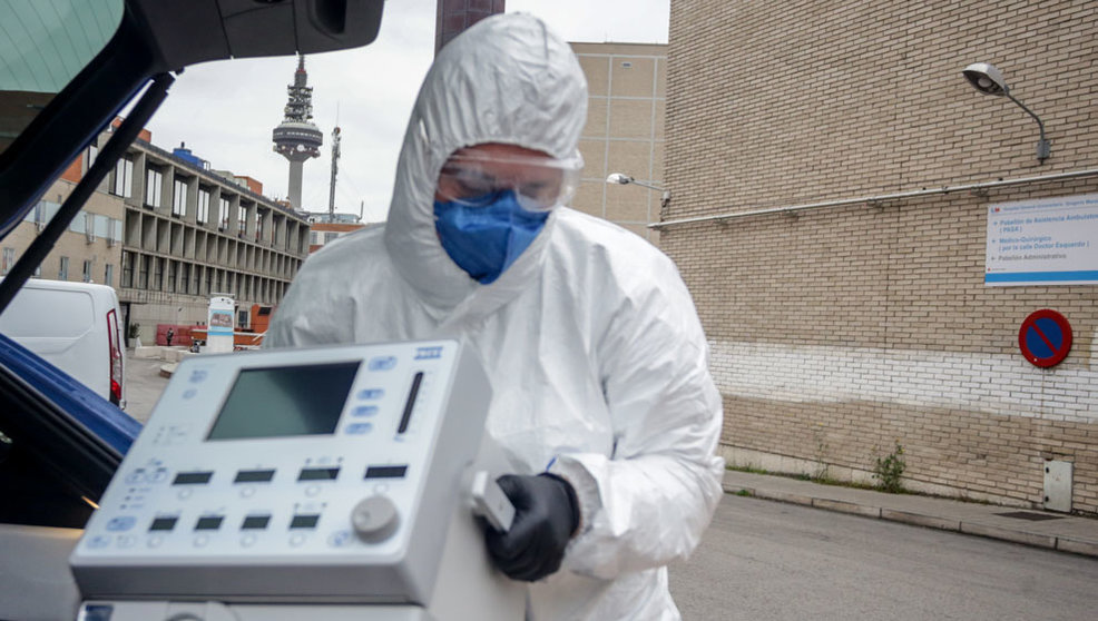 Un técnico protegido con un traje, guantes y mascarilla en el Hospital Gregorio Marañón, saca un respirador del maletero de su coche