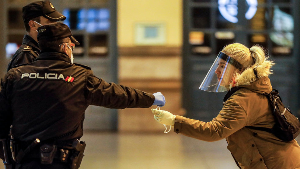 Un policía nacional entrega una mascarilla a una mujer en el vestíbulo de la estación del Norte de Valencia