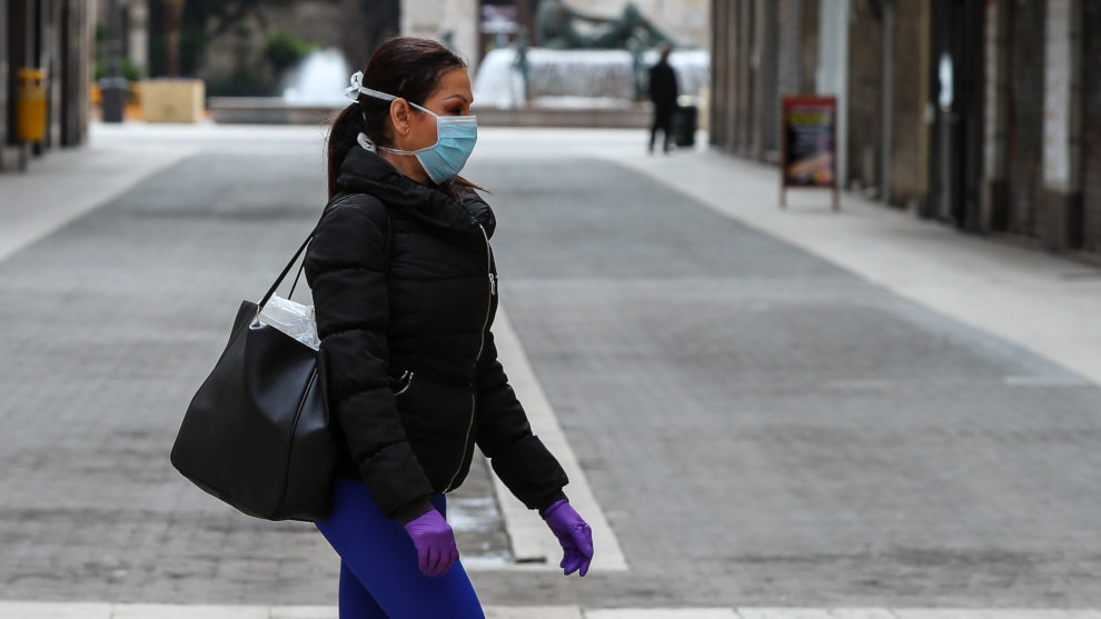 Una mujer camina con mascarilla y guantes de látex