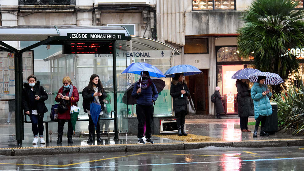 Varias personas con paraguas esperan en una estación de autobús en Santander