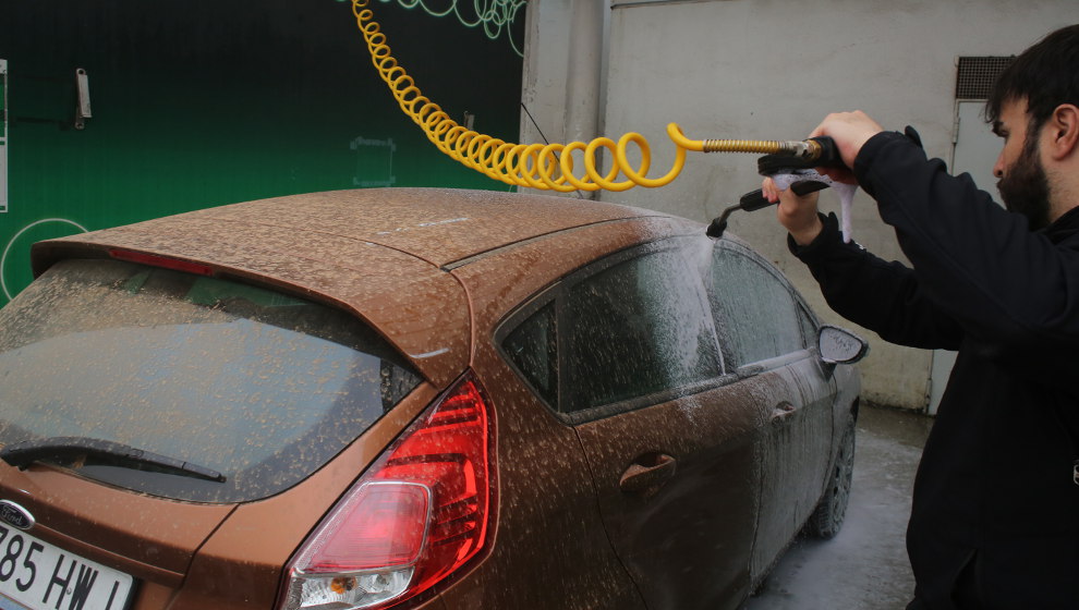 Un hombre lava su vehículo tras estar cubierto de polvo sahariano